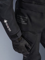 Jaqueta Alpinestars Stella ST-7 2L GORE-TEX Feminina, jaqueta de aventura e touring preta, vista em pormenor da manga com logótipo GORE-TEX branco, texto 'Alpinestars Exploration Equipment' na zona da anca, luva de motociclismo preta, material têxtil impermeável com bolsos de carga funcionais