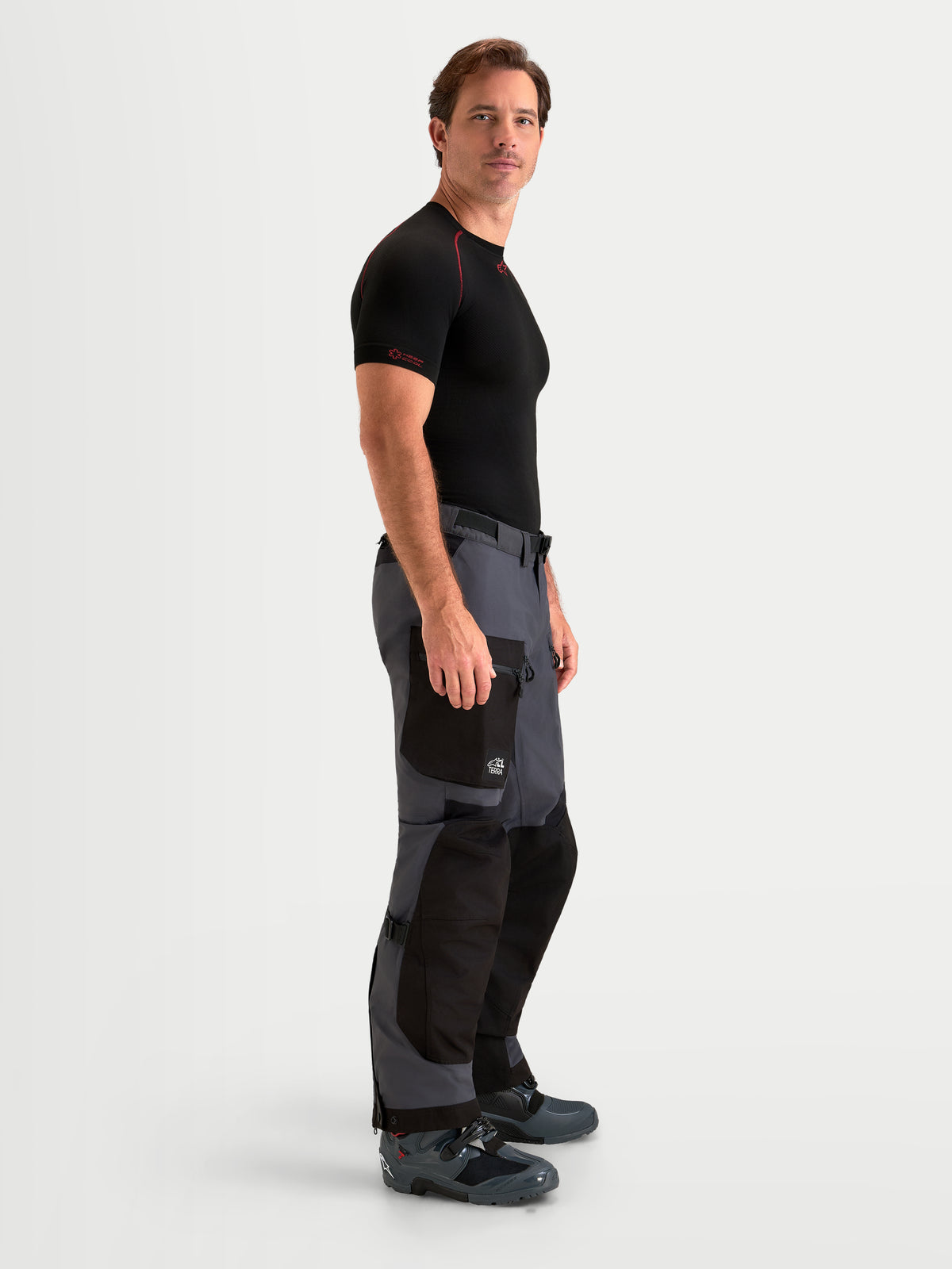 Alpinestars Arenis Gore-Tex calças de moto adventure para homem em preto e cinzento escuro, vista de perfil lateral num modelo a mostrar a construção têxtil impermeável e o bolso cargo