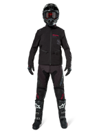 Motocross rider wearing the Alpinestars Lite-Dura Softshell Jacket in Black with red logo details, styled with matching black off-road pants, black helmet, and white and black boots, complete professional enduro racing gear.