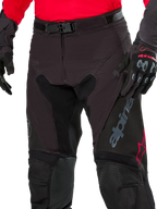 Close-up of Alpinestars Pro-Dura Pants, Enduro Pants, Black Magnet White with red accents, featuring a secure magnetic buckle closure and zip fly, worn with matching red jersey and black gloves, durable ripstop construction for off-road riding