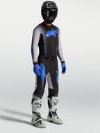 Alpinestars Supertech Hiten AFD, calças de motocross para homem, pretas e azuis, em modelo com camisola e botas brancas.