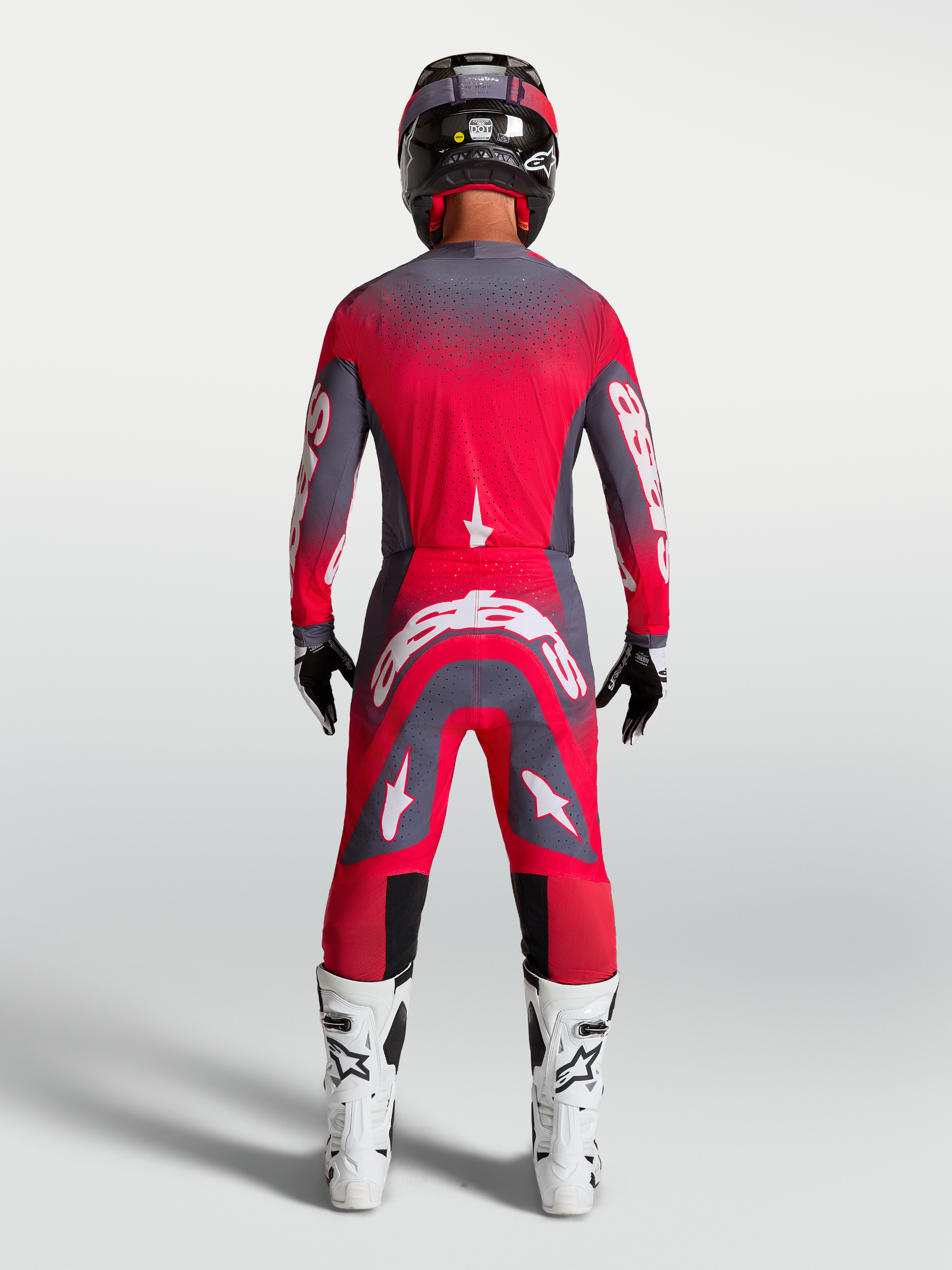 Alpinestars Supertech Hiten AFD Gear Set e calças, equipamento de corrida de motocross para homem, vermelho fluorescente e cinzento, vista traseira no modelo com botas e capacete.