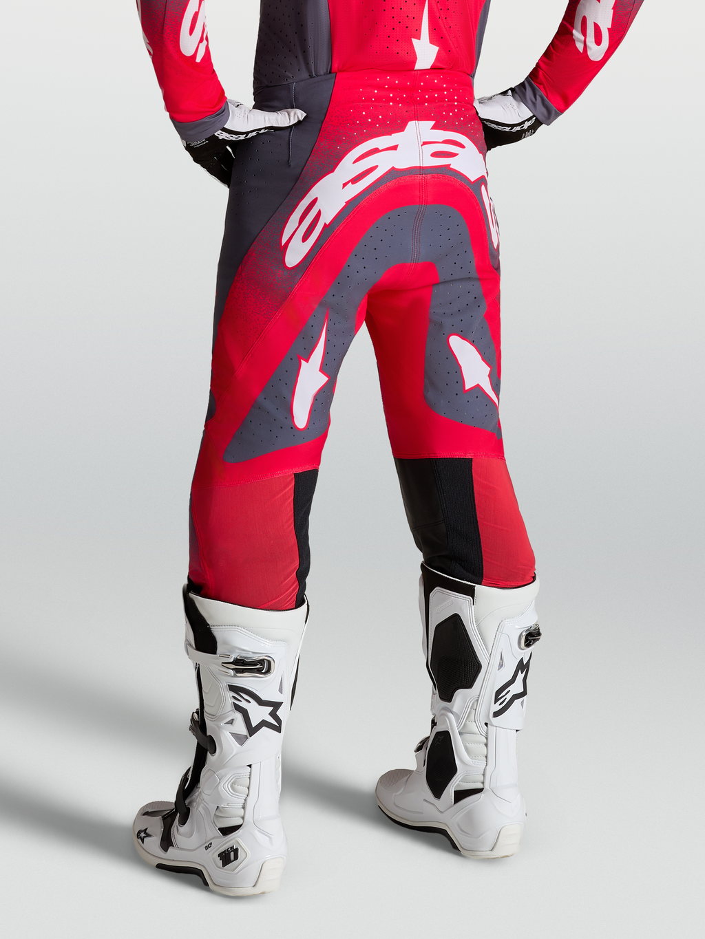 Alpinestars Supertech Hiten AFD, calças de motocross vermelhas e cinzentas, vista traseira, com botas de corrida brancas.