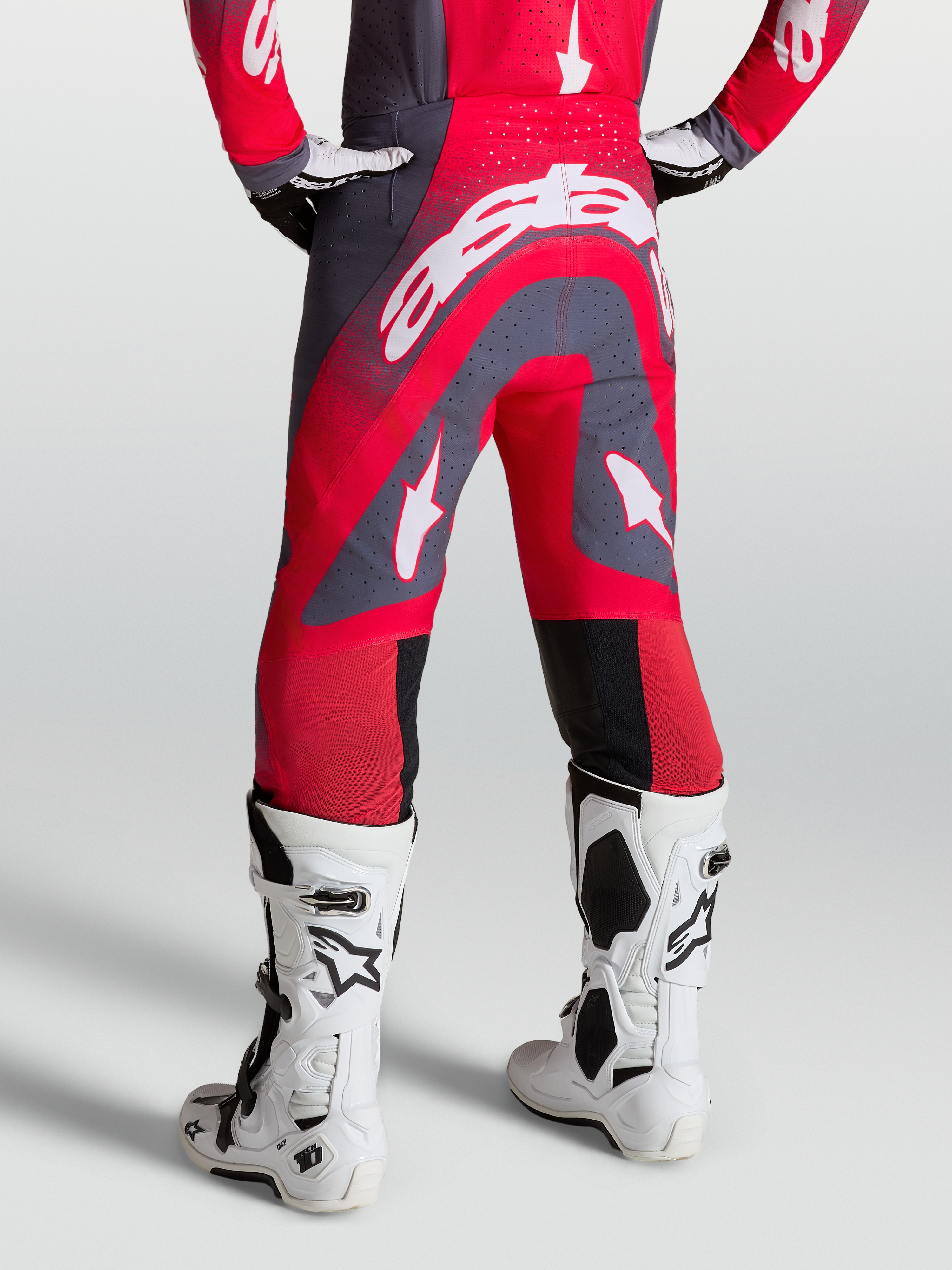 Alpinestars Supertech Hiten AFD, calças de motocross vermelhas e cinzentas, vista traseira, com botas de corrida brancas.