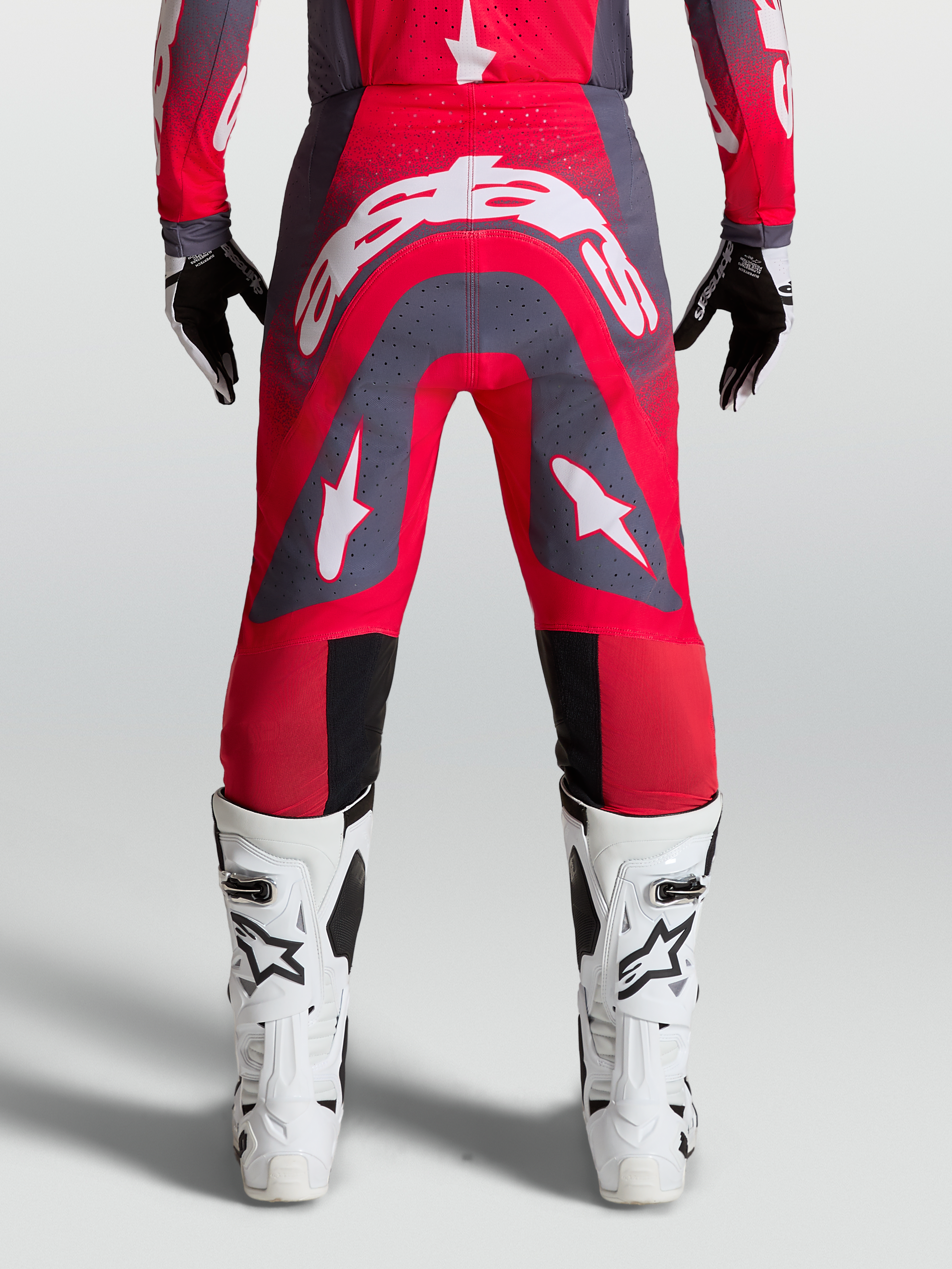 Alpinestars Supertech Hiten AFD, calças de motocross profissionais, vermelho fluorescente e cinzento, vista traseira em modelo com logótipo branco, equipamento de corrida todo-o-terreno