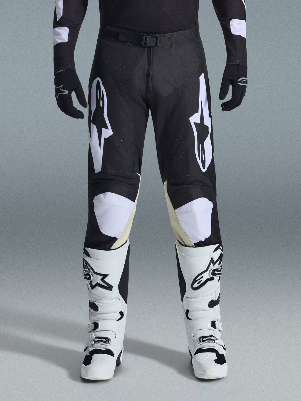 Alpinestars 2026 Racer Air Riway Pants, calças de motocross, pretas e brancas, com logótipos Alpinestars brancos em destaque nas coxas e nos painéis dos joelhos, combinadas com botas de motocross brancas e pretas e luvas pretas, design de ajuste desportivo de corrida para condução off-road