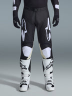 Alpinestars 2026 Racer Air Riway Pants, calças de motocross, pretas e brancas, com logótipos Alpinestars brancos em destaque nas coxas e nos painéis dos joelhos, combinadas com botas de motocross brancas e pretas e luvas pretas, design de ajuste desportivo de corrida para condução off-road
