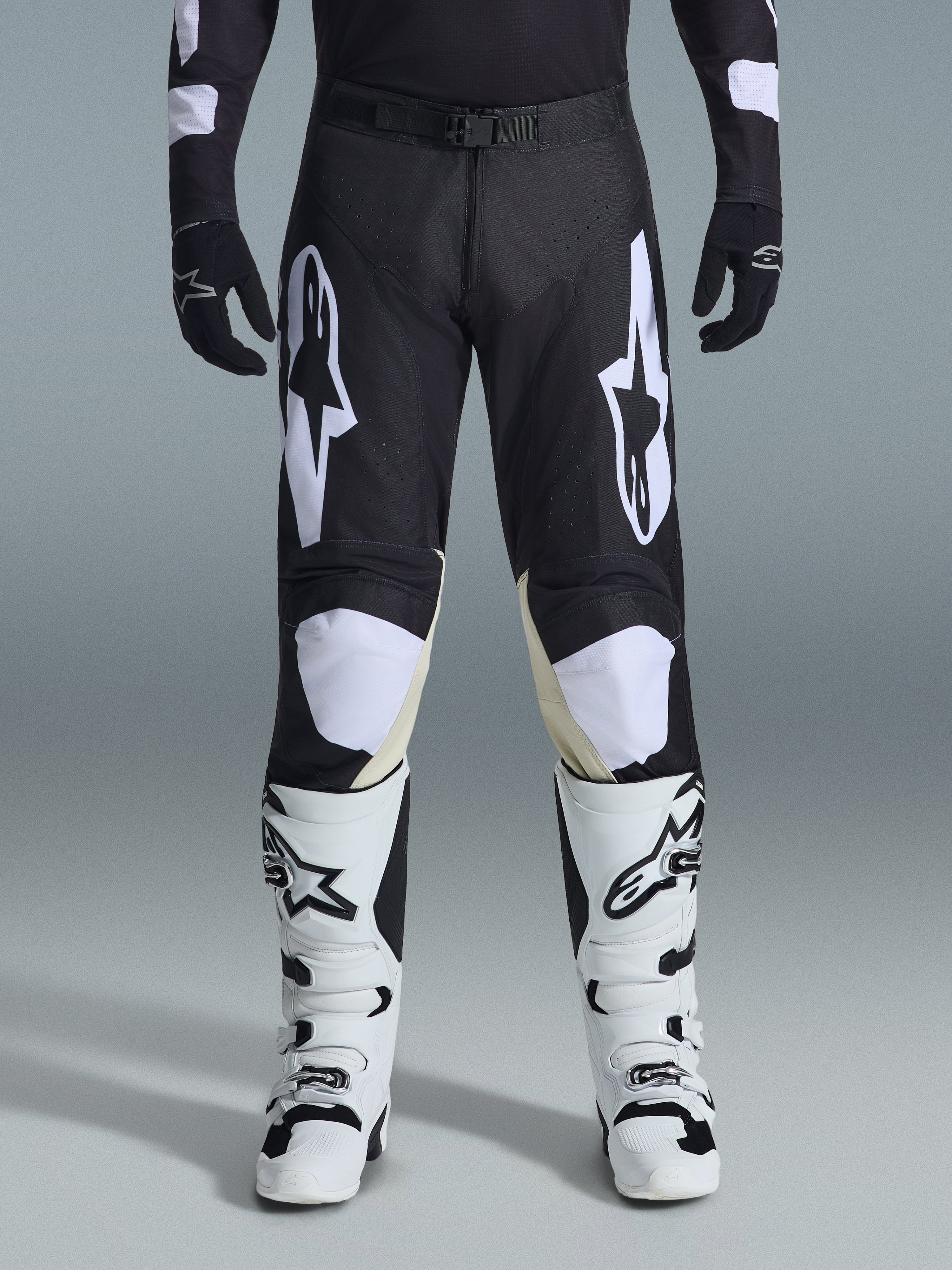 Alpinestars 2026 Racer Air Riway Pants, calças de motocross, pretas e brancas, com logótipos Alpinestars brancos em destaque nas coxas e nos painéis dos joelhos, combinadas com botas de motocross brancas e pretas e luvas pretas, design de ajuste desportivo de corrida para condução off-road