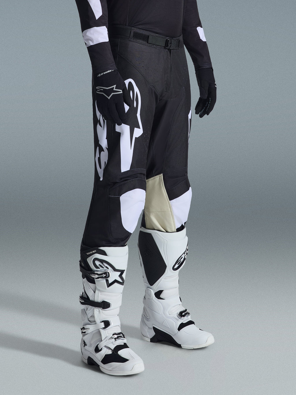 Calças Alpinestars 2026 Racer Air Riway, calças de motocross, pretas e brancas, usadas com botas Tech Series brancas e pretas e camisola preta de manga comprida, com marca Alpinestars branca, perfurações cortadas a laser e painéis internos nos joelhos em couro de cabra bege para performance off-road