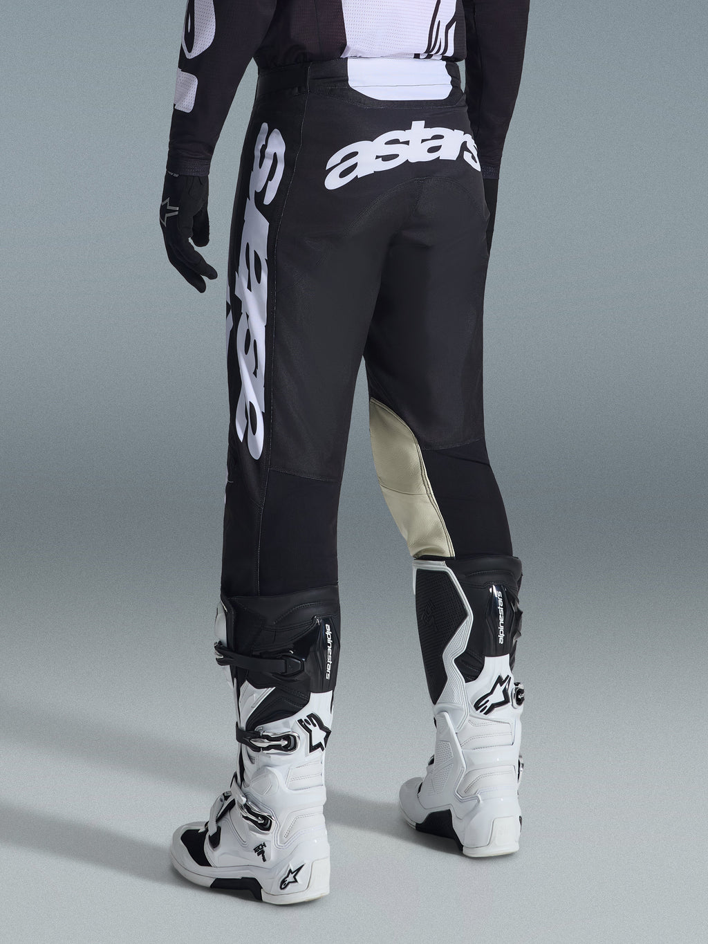 Calças Alpinestars 2026 Racer Air Riway, calças de motocross, pretas e brancas, vista traseira com branding Astars grande em branco no assento e nas pernas, painéis internos dos joelhos em couro bege, usadas com botas Tech 7 brancas e pretas, vestuário de corrida off-road premium