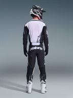 Piloto de motocross visto de costas a usar calças Alpinestars 2026 Racer Air Riway em preto e branco, camisola de manga comprida preta e branca a condizer, botas de competição brancas e pretas e capacete preto com a marca Alpinestars