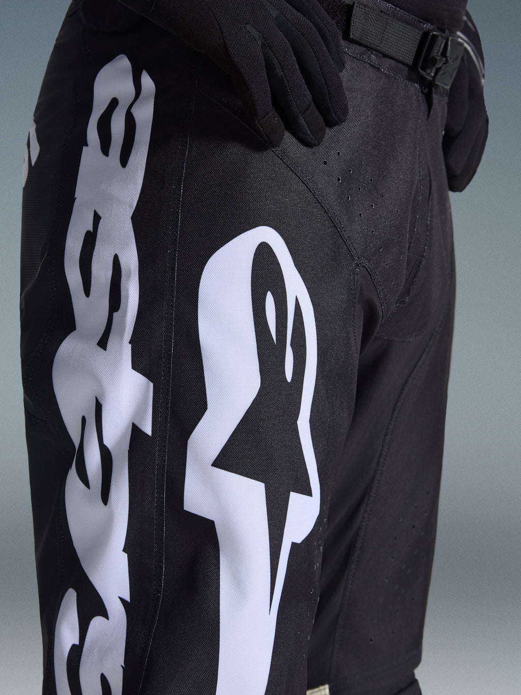 Alpinestars 2026 Racer Air Riway Pants, calças de motocross, pretas e brancas, pormenor com branding Alpinestars grande em branco, perfurações cortadas a laser para fluxo de ar e fivela de cintura ajustável, tecido durável para condução off-road
