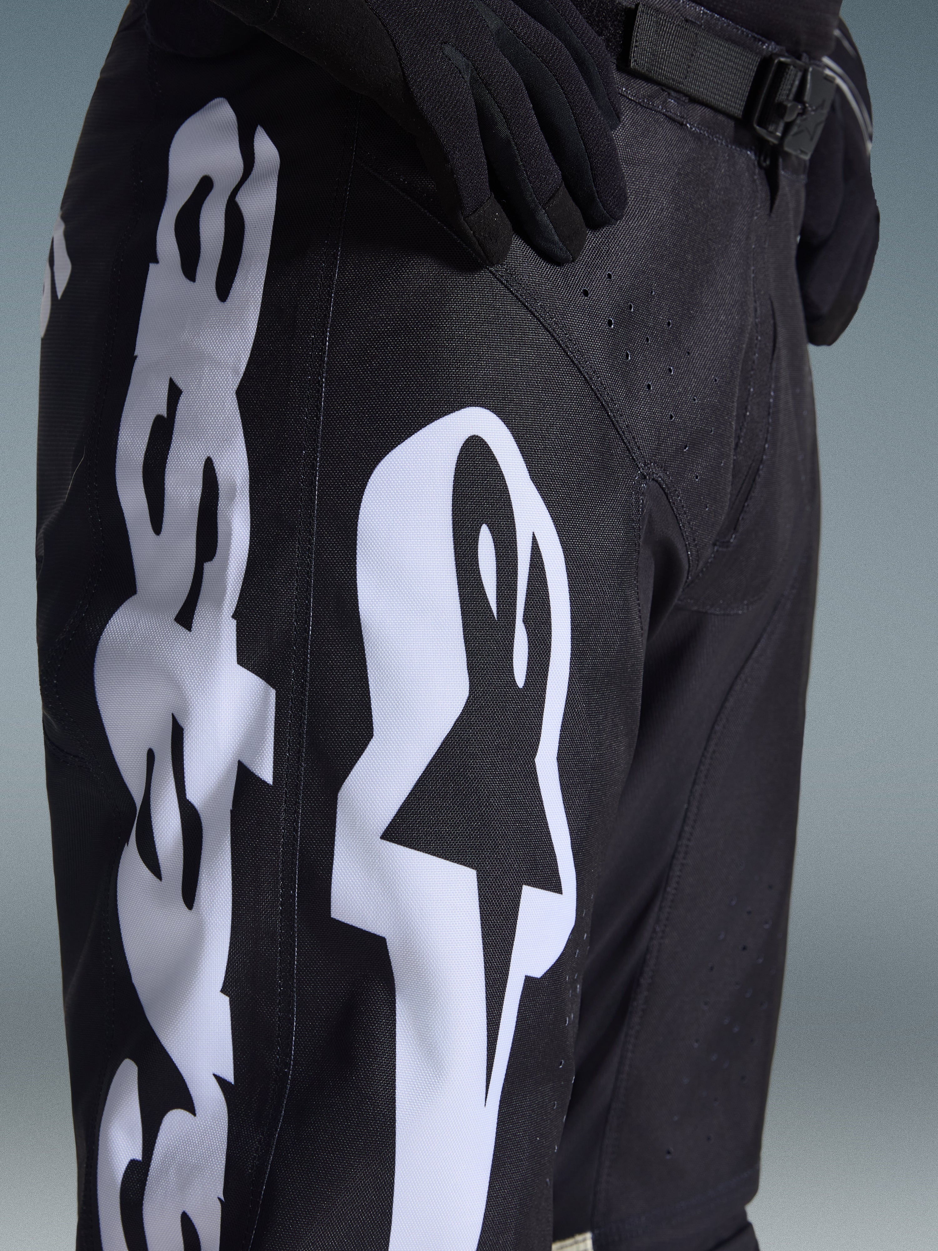 Alpinestars 2026 Racer Air Riway Pants, calças de motocross, pretas e brancas, pormenor com branding Alpinestars grande em branco, perfurações cortadas a laser para fluxo de ar e fivela de cintura ajustável, tecido durável para condução off-road