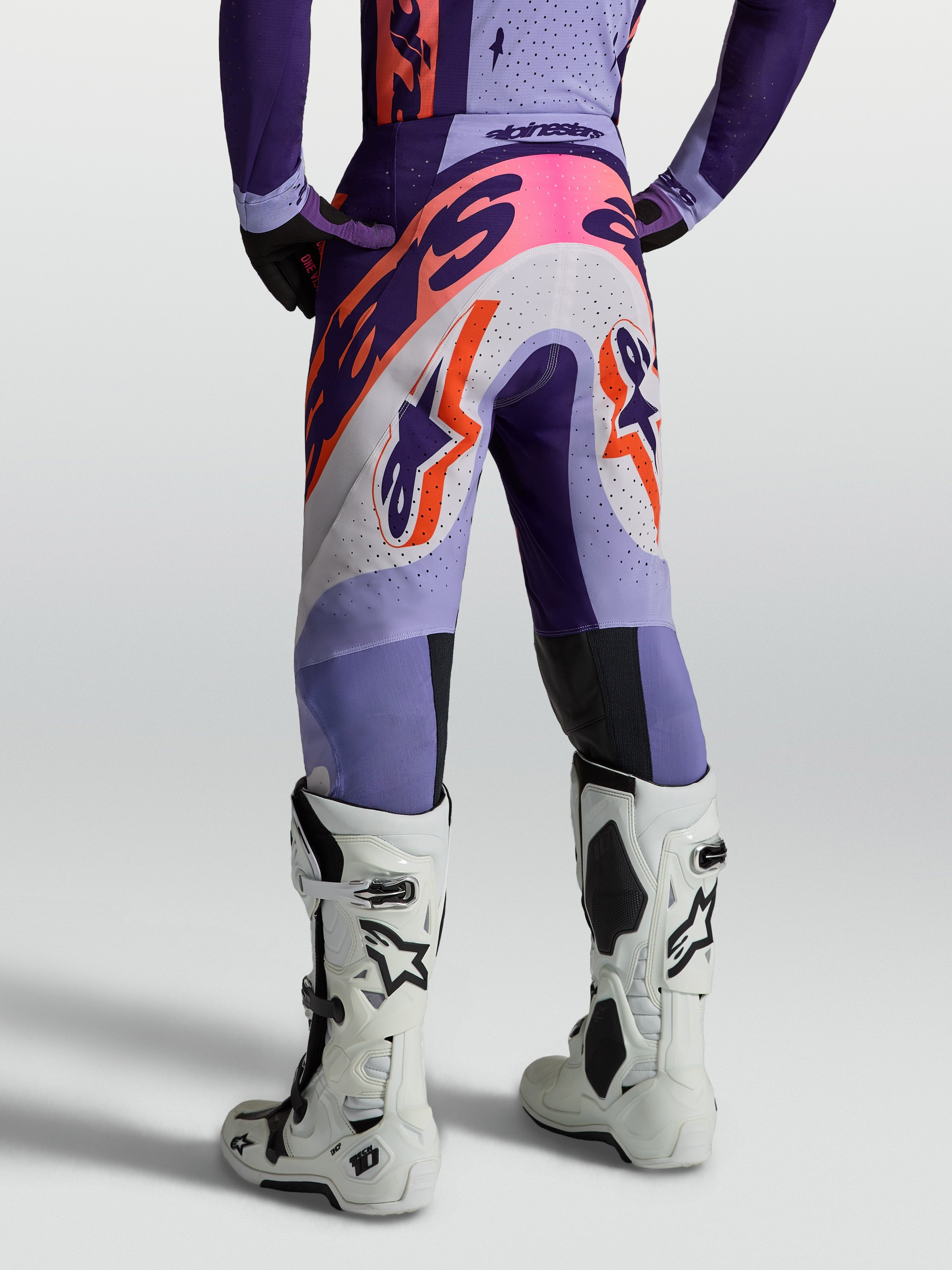 Alpinestars Supertech Dyna, calças de motocross para homem, roxo e violeta com detalhes rosa fluo, vista traseira em modelo, construção em tecido elástico respirável para alto desempenho