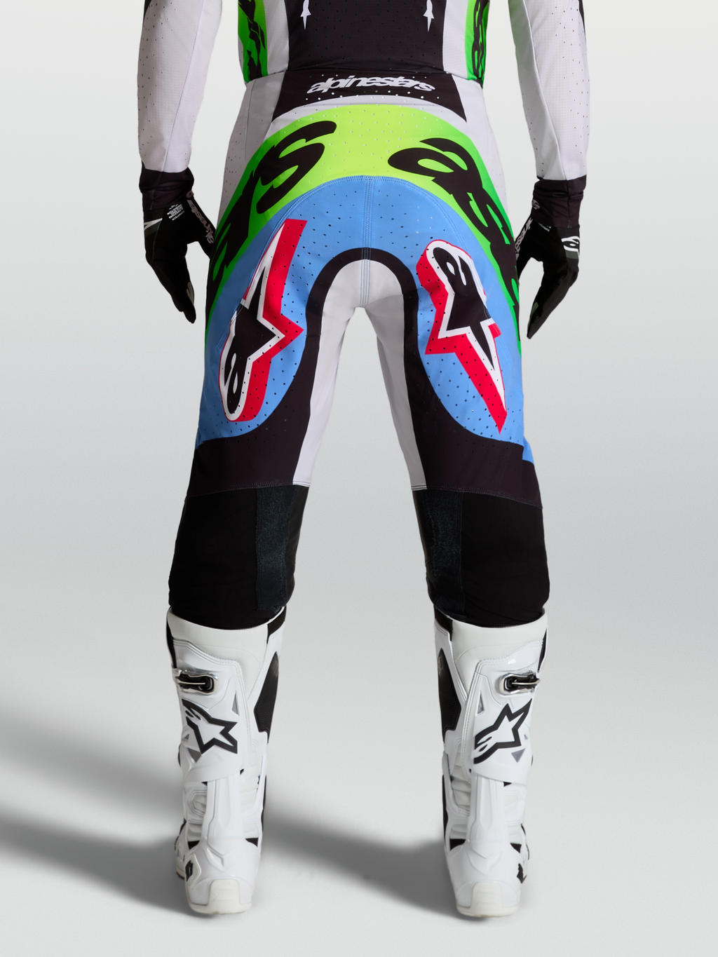 Alpinestars calças Supertech Dyna, calças de motocross para homem, vista traseira lilás e verde fluo com painéis perfurados.