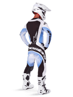 Piloto de motocross visto de costas a usar calças e camisola Alpinestars 2025 Techstar Melt, design com degradê em preto, azul e branco, capacete branco, botas brancas e pretas, equipamento completo de competição para todo-o-terreno