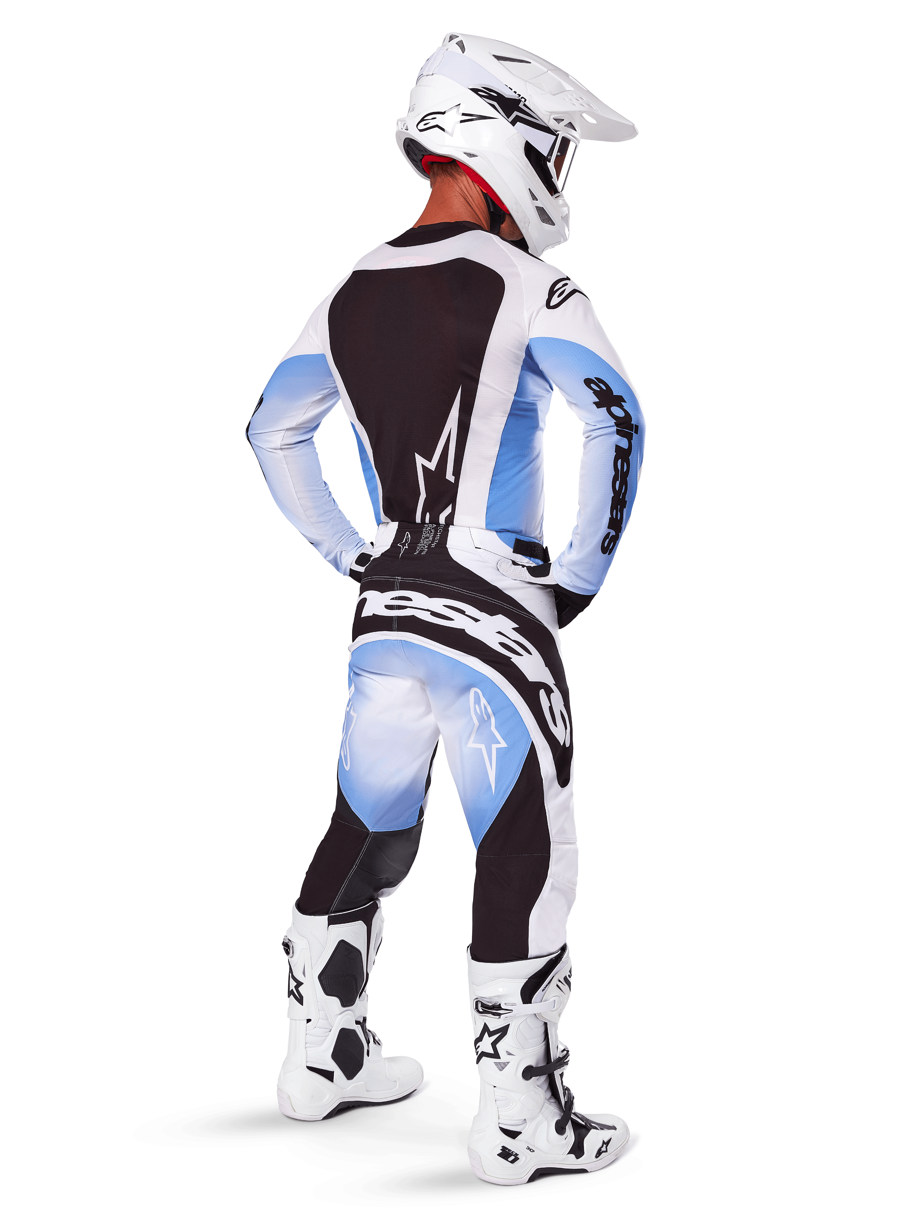 Piloto de motocross visto de costas a usar calças e camisola Alpinestars 2025 Techstar Melt, design com degradê em preto, azul e branco, capacete branco, botas brancas e pretas, equipamento completo de competição para todo-o-terreno