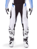 Alpinestars 2025 Techstar Melt Pants, calças de motocross, brancas e pretas com detalhes em azul claro, usadas com botas e luvas a condizer em branco e preto, com perfurações a laser e design de competição de alto desempenho
