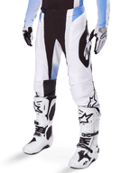 Alpinestars 2025 Techstar Melt Pants, calças de motocross, brancas e pretas com detalhes azuis, com perfurações a laser para ventilação e construção de joelho Babel, usadas com botas e luvas de motocross brancas a condizer, design atlético de corrida todo-o-terreno