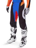 Alpinestars 2025 Techstar Melt Pants, calças de motocross, pretas com detalhes azuis e laranja, usadas com botas brancas e camisola a condizer, com material de proteção durável e um design desportivo de corrida
