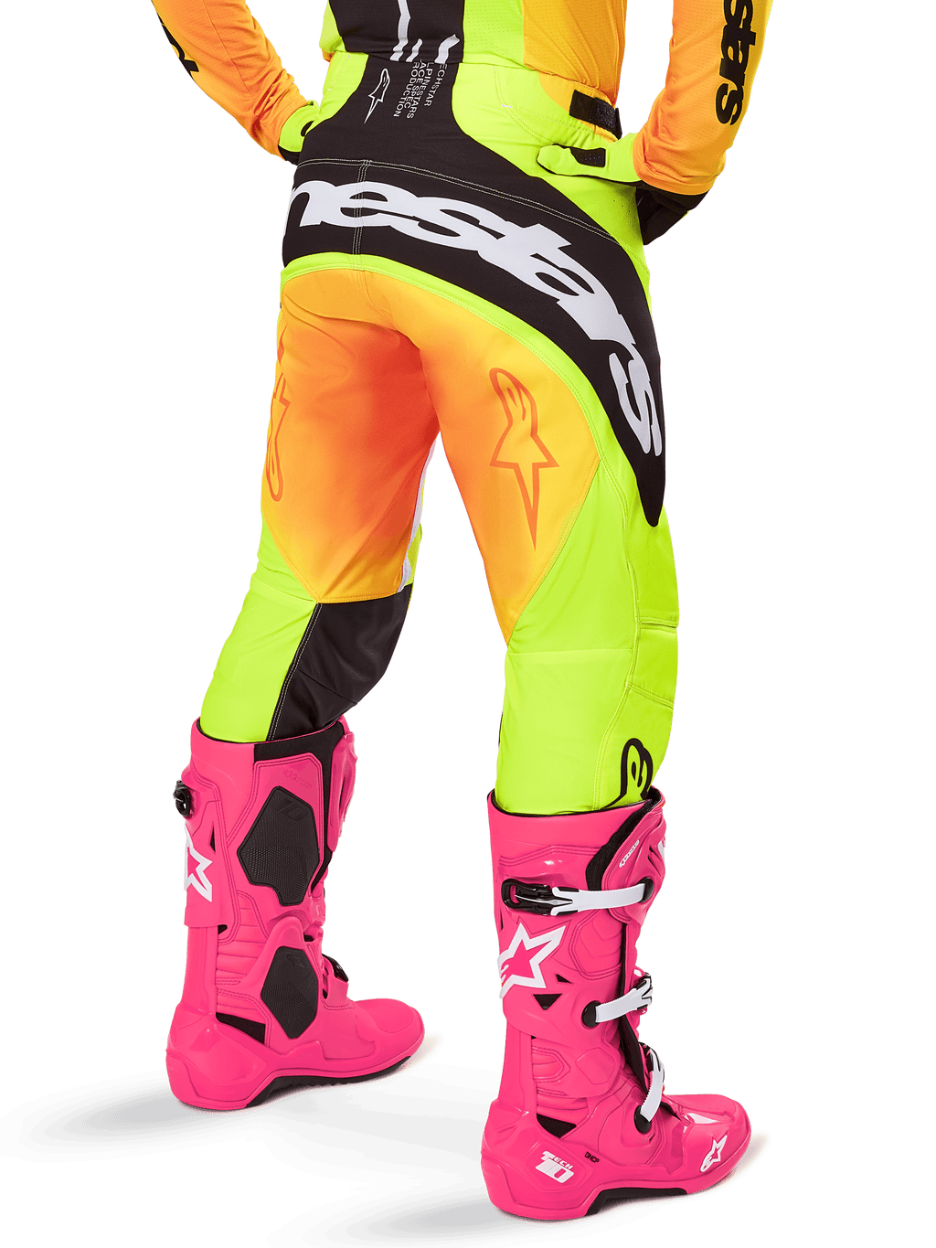 Vista traseira de um piloto de motocross com calças Alpinestars 2025 Techstar Melt, gradiente amarelo e laranja com logótipo preto e branco no assento, combinadas com botas de motocross cor-de-rosa vibrante, equipamento de performance para todo-o-terreno.