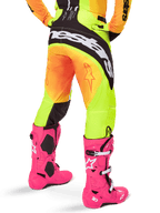 Vista traseira de um piloto de motocross com calças Alpinestars 2025 Techstar Melt, gradiente amarelo e laranja com logótipo preto e branco no assento, combinadas com botas de motocross cor-de-rosa vibrante, equipamento de performance para todo-o-terreno.