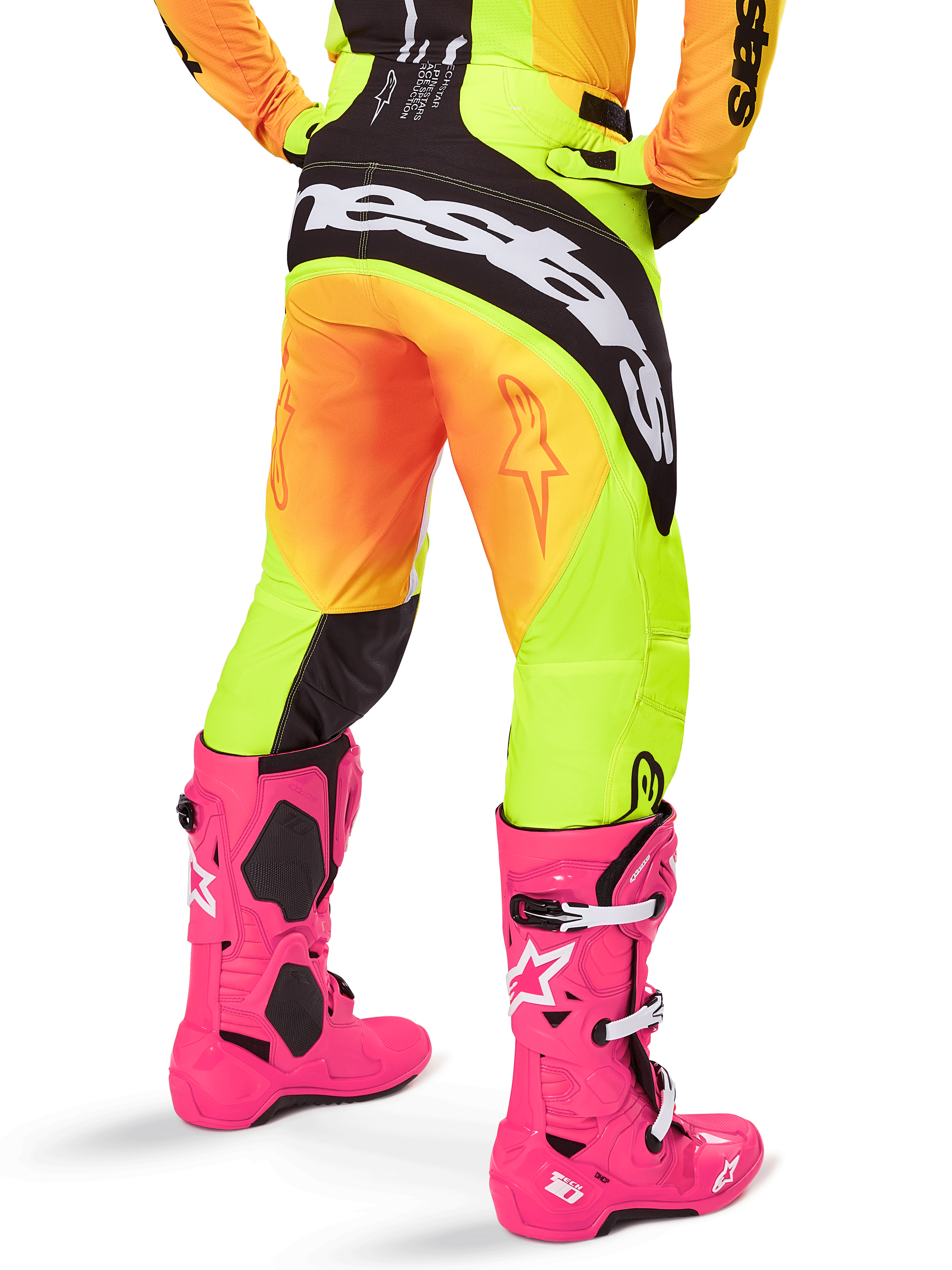 Vista traseira de um piloto de motocross com calças Alpinestars 2025 Techstar Melt, gradiente amarelo e laranja com logótipo preto e branco no assento, combinadas com botas de motocross cor-de-rosa vibrante, equipamento de performance para todo-o-terreno.