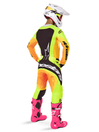 Piloto de motocross visto de trás com o Conjunto de Equipamento Alpinestars 2025 Techstar Melt, camisola e calças com gradiente amarelo e laranja e painéis pretos, capacete branco com óculos vermelhos, botas cor-de-rosa vibrante, conjunto de corrida coordenado para performance todo-o-terreno