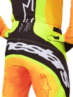 Alpinestars 2025 Techstar Melt Pants, calças de motocross, pormenor da vista traseira, amarelo néon e laranja com painéis pretos, logótipo Alpinestars grande a branco na zona do assento, equipamento de condução off-road de alta performance