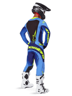 Alpinestars 2025 Techstar Melt Pants, equipamento de motocross, Amarelo Fluo Azul, vista traseira de piloto com camisola azul a condizer e marca amarela grande, botas brancas e pretas e capacete preto, conjunto de corrida coordenado para desempenho off-road