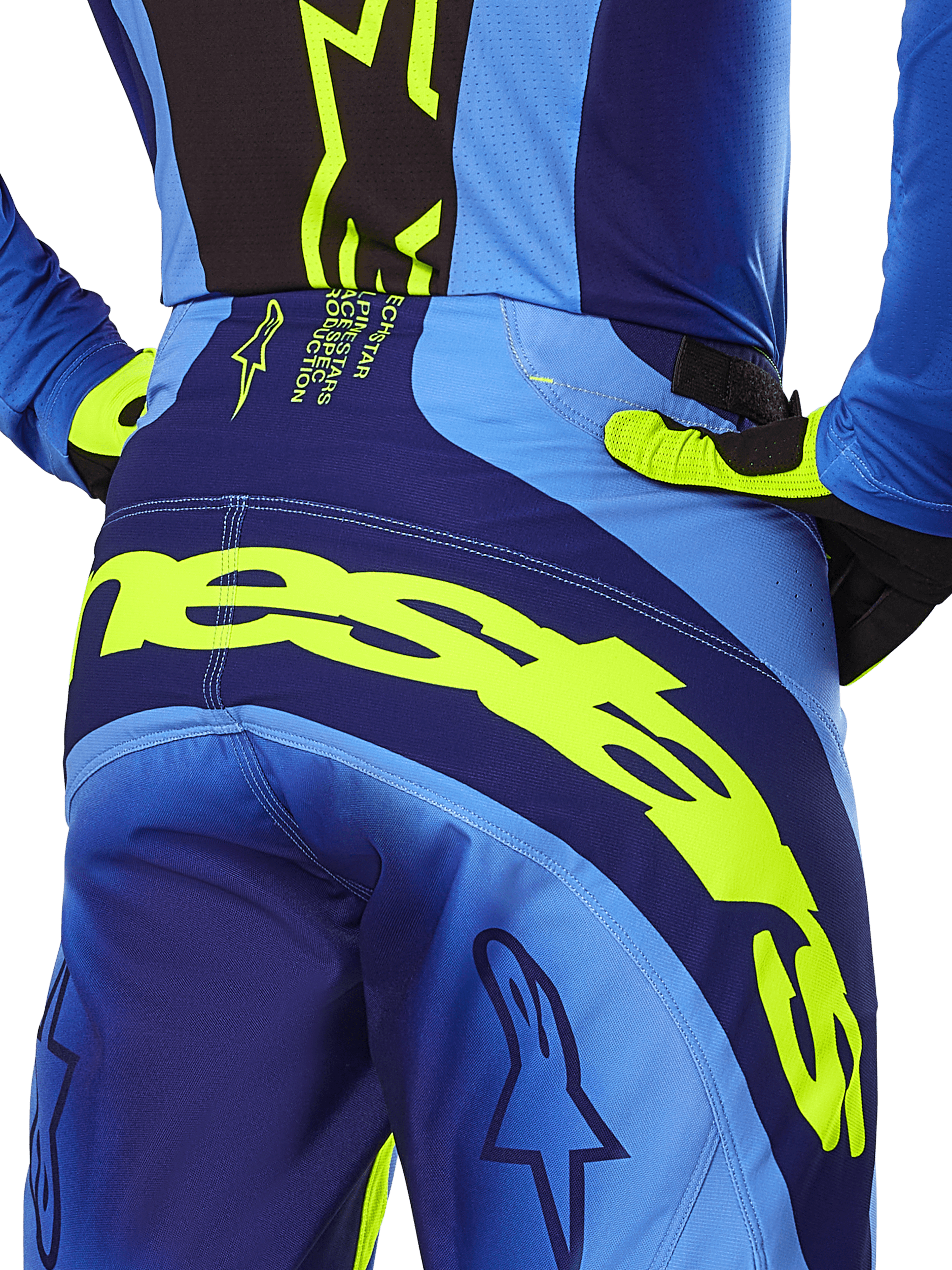 Alpinestars 2025 Techstar Melt Pants, calças de motocross, amarelo néon e azul, pormenor da vista traseira com logótipo Alpinestars em amarelo em destaque no assento, usadas com camisola azul a condizer e luvas amarelo néon, concebidas para performance em corridas fora de estrada.