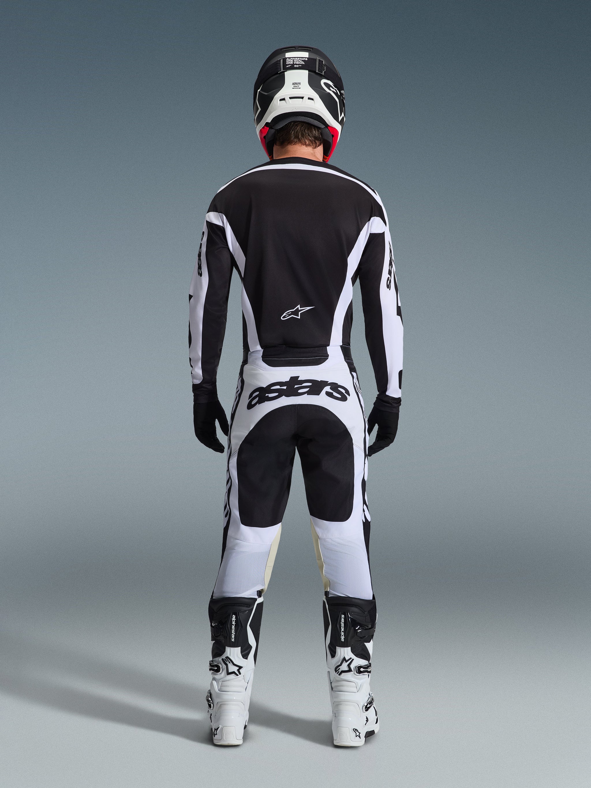 Calças Alpinestars 2026 Racer Riway, calças de motocross, brancas e pretas, vista traseira do conjunto completo de equipamento de corrida, marca 'astars' em destaque no assento, usadas com camisola a condizer, botas brancas e capacete preto, conjunto de corrida off-road coordenado.