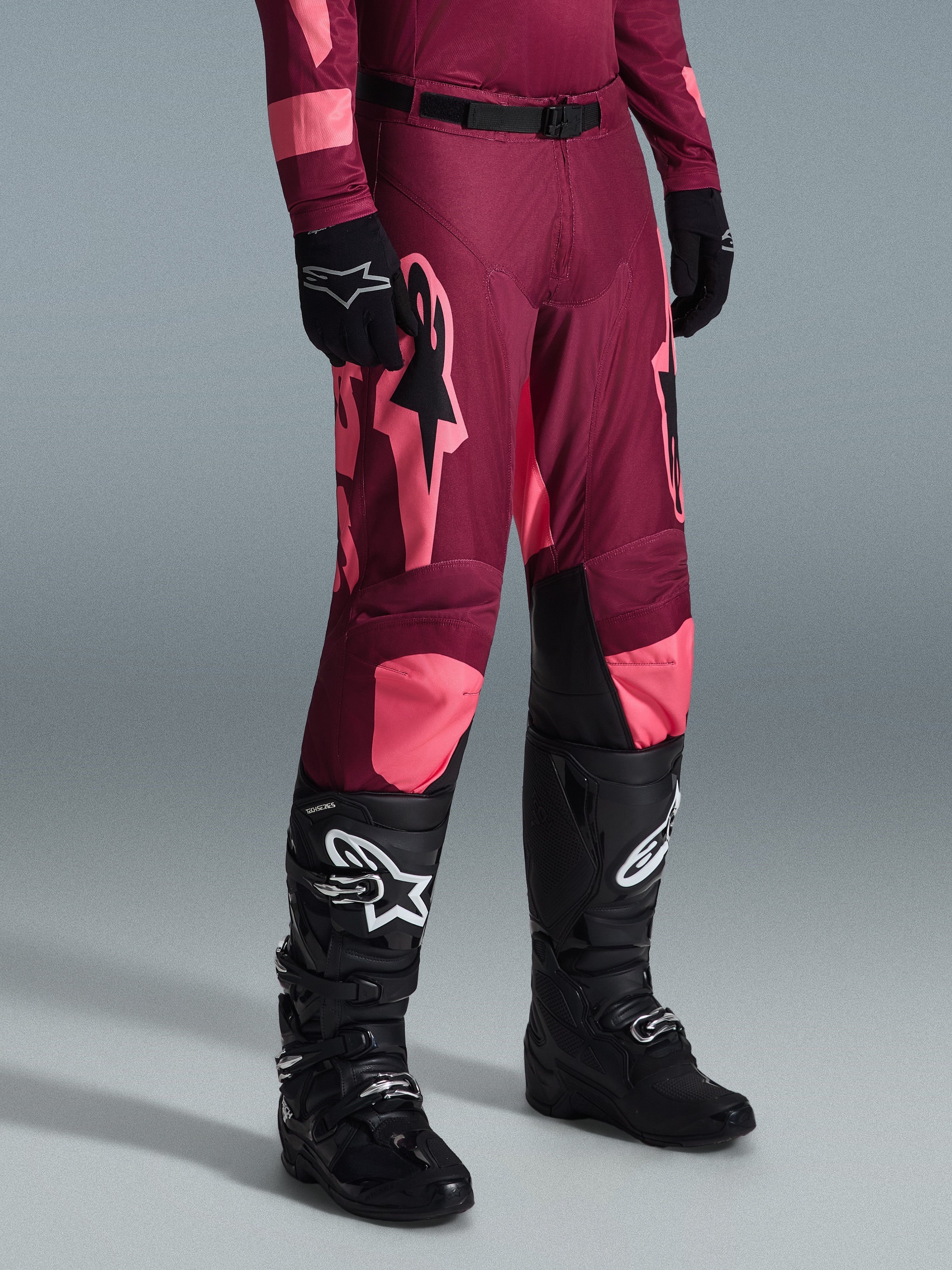 Alpinestars 2026 Racer Riway Pants, calças de motocross, Dark Red Coral, com grandes logótipos de estrela cor-de-rosa e painéis internos nos joelhos em preto, combinadas com botas de motocross pretas e luvas pretas, corte atlético de corrida para condução off-road