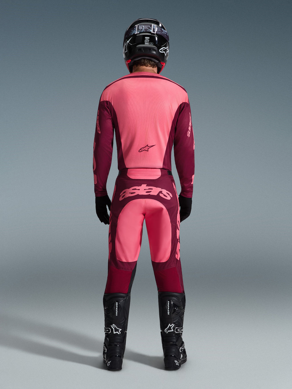 Piloto de motocross visto de costas a usar a camisola Alpinestars 2026 Racer Riway e calças a condizer em Dark Red Coral, com botas pretas, capacete preto e luvas pretas, equipamento de alto desempenho coordenado para todo-o-terreno