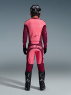 Piloto de motocross visto de costas a usar a camisola Alpinestars 2026 Racer Riway e calças a condizer em Dark Red Coral, com botas pretas, capacete preto e luvas pretas, equipamento de alto desempenho coordenado para todo-o-terreno