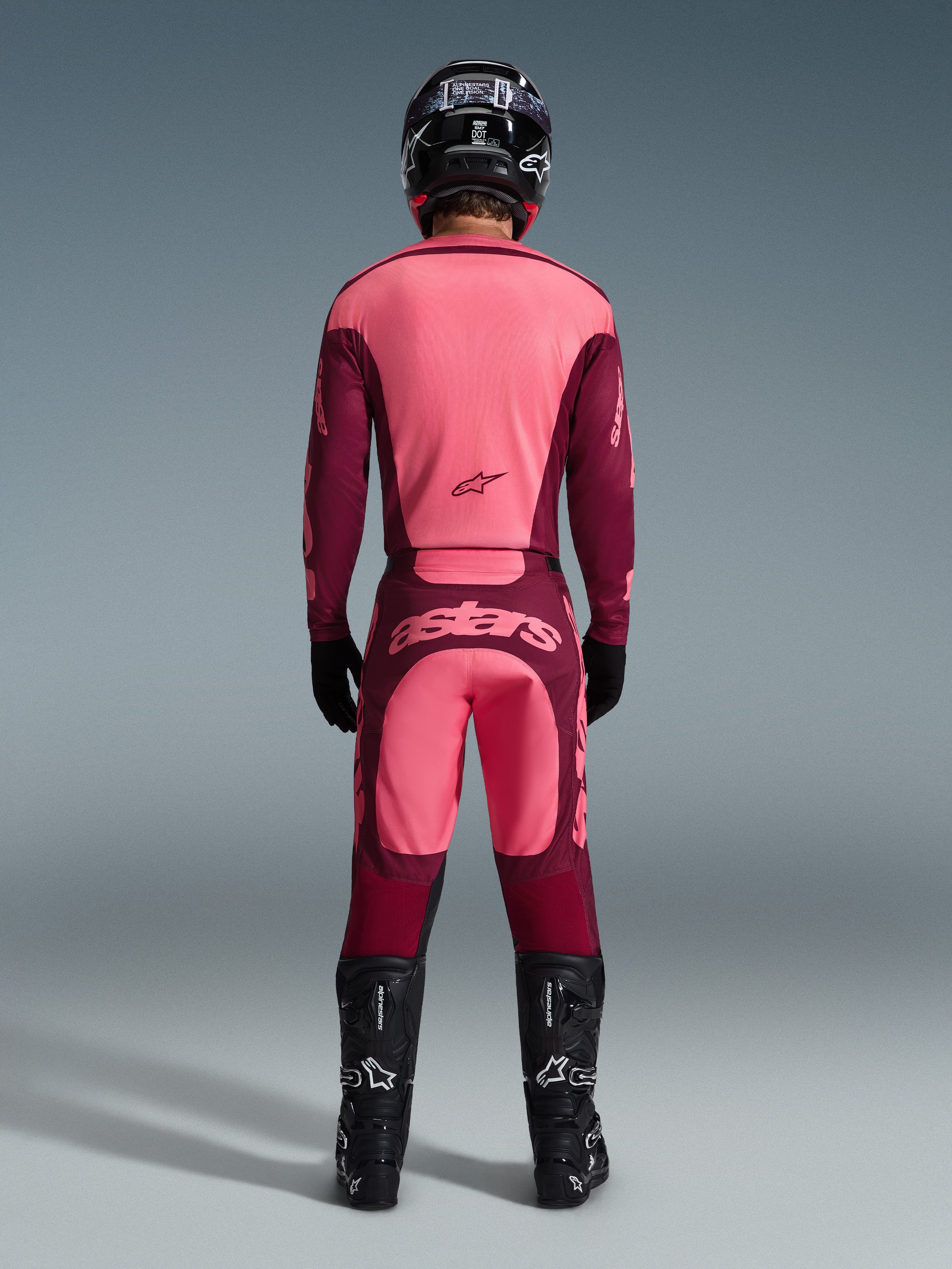 Piloto de motocross visto de costas a usar a camisola Alpinestars 2026 Racer Riway e calças a condizer em Dark Red Coral, com botas pretas, capacete preto e luvas pretas, equipamento de alto desempenho coordenado para todo-o-terreno