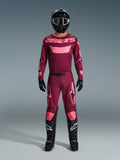 Piloto de motocross com o Conjunto de Equipamento Alpinestars 2026 Racer Riway, camisola bordeaux com marca 'astars' em cor-de-rosa, calças bordeaux a condizer com detalhes rosa nos joelhos e pernas, capacete preto, luvas pretas e botas pretas, conjunto de performance completo para corridas todo-o-terreno