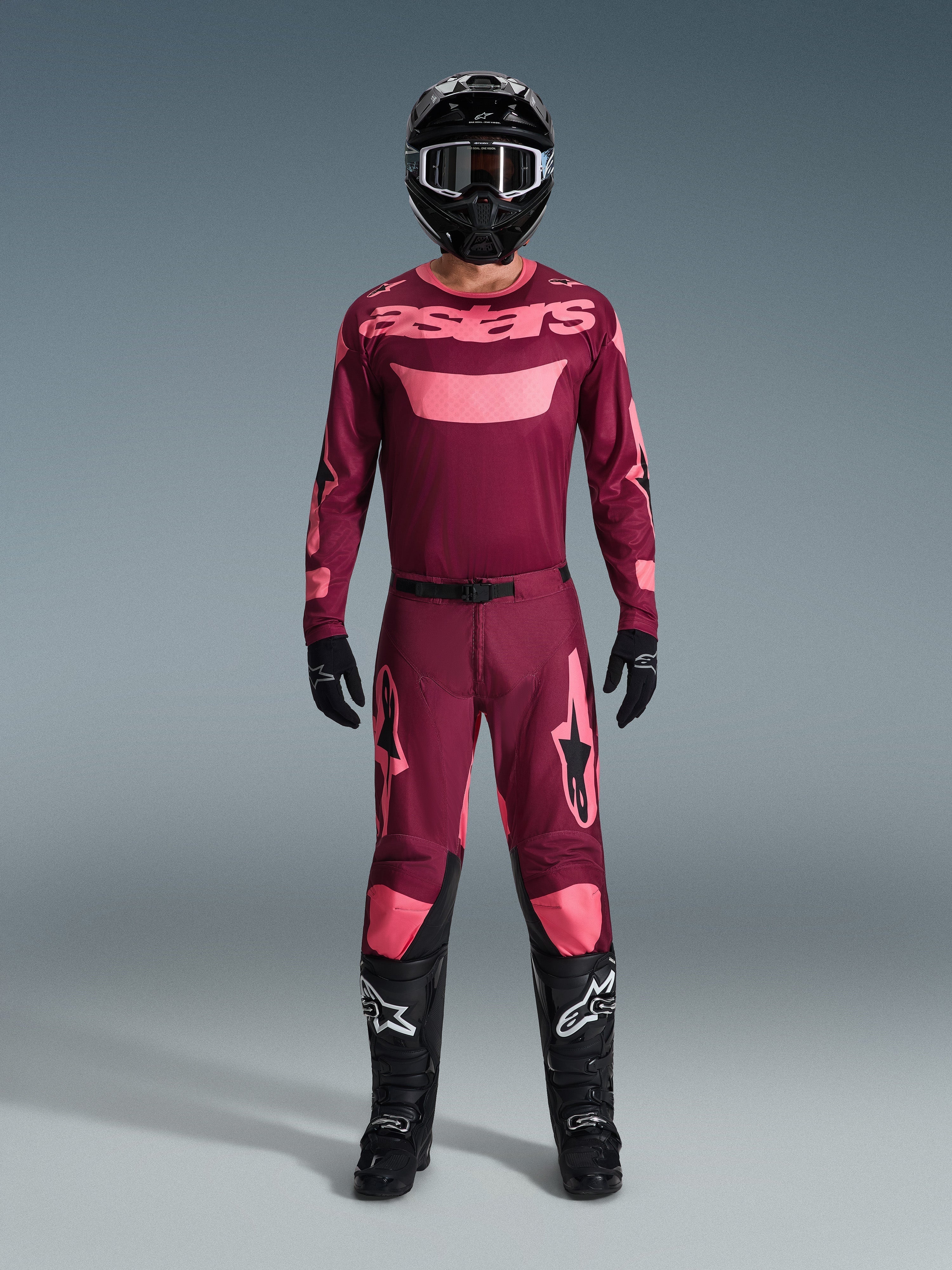 Piloto de motocross com equipamento de corrida completo, Camisola Racer Riway 2026 em Dark Red Coral, calças em vermelho escuro com detalhes coral a condizer, capacete preto com detalhes brancos, botas pretas com logótipos brancos e luvas pretas, conjunto coordenado para corridas off-road