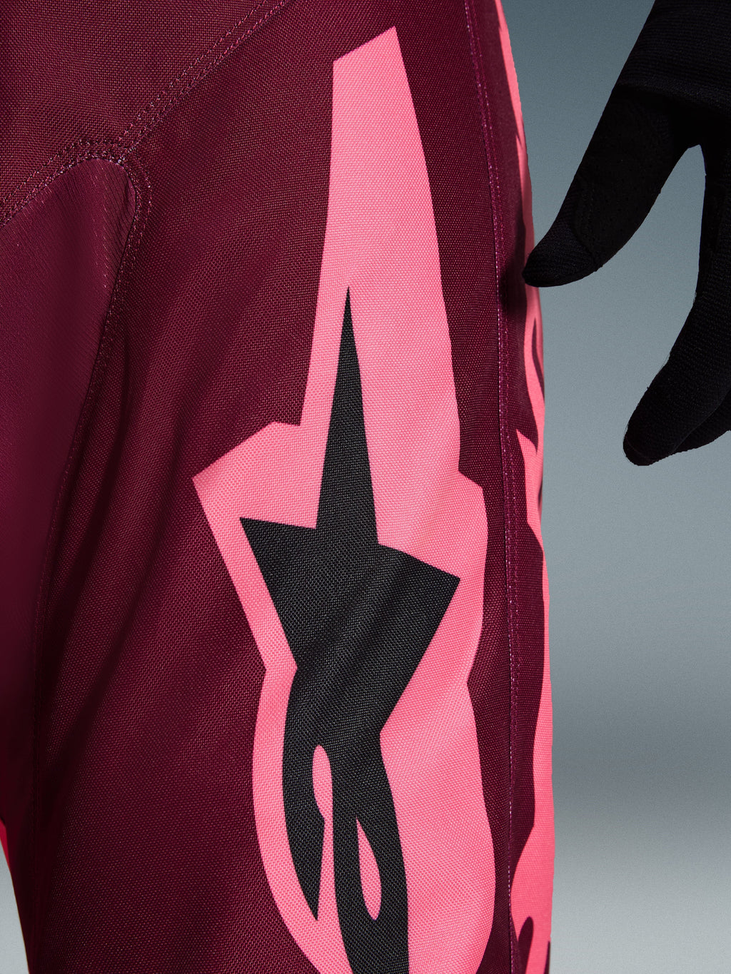 Calças Alpinestars 2026 Racer Riway, calças de motocross, Dark Red Coral, vista de pormenor com um grande gráfico angular rosa coral e logótipo de estrela preto, destacando a textura do tecido durável e as costuras de performance