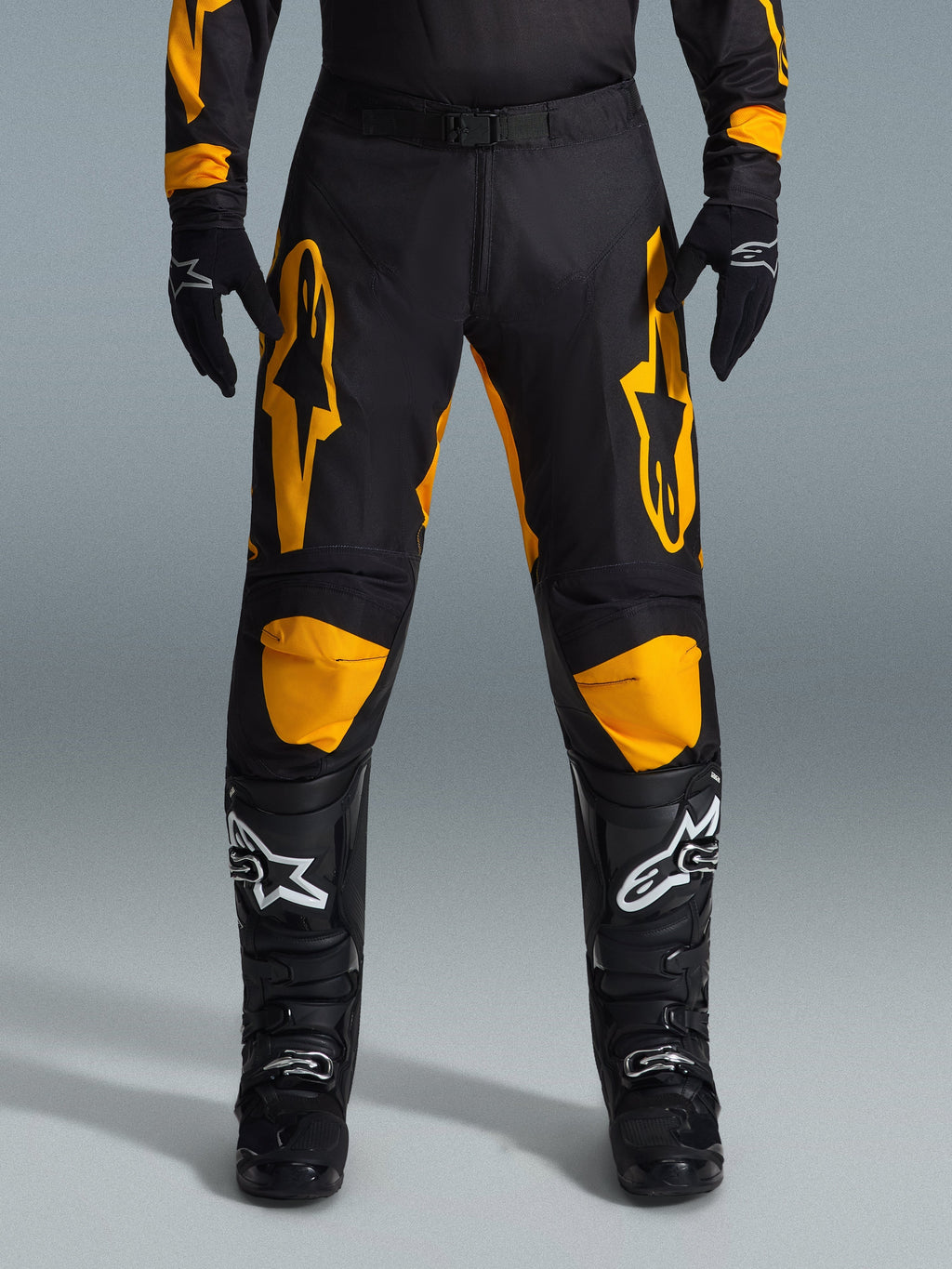 Calças Alpinestars 2026 Racer Riway, calças de motocross, amarelas e pretas, usadas com luvas de motocross pretas e botas pretas com logótipos brancos, com grandes logótipos Alpinestars amarelos nas coxas e painéis amarelos nos joelhos, design durável para desempenho em corridas todo-o-terreno