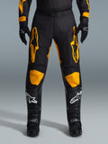 Calças Alpinestars 2026 Racer Riway, calças de motocross, amarelas e pretas, usadas com luvas de motocross pretas e botas pretas com logótipos brancos, com grandes logótipos Alpinestars amarelos nas coxas e painéis amarelos nos joelhos, design durável para desempenho em corridas todo-o-terreno