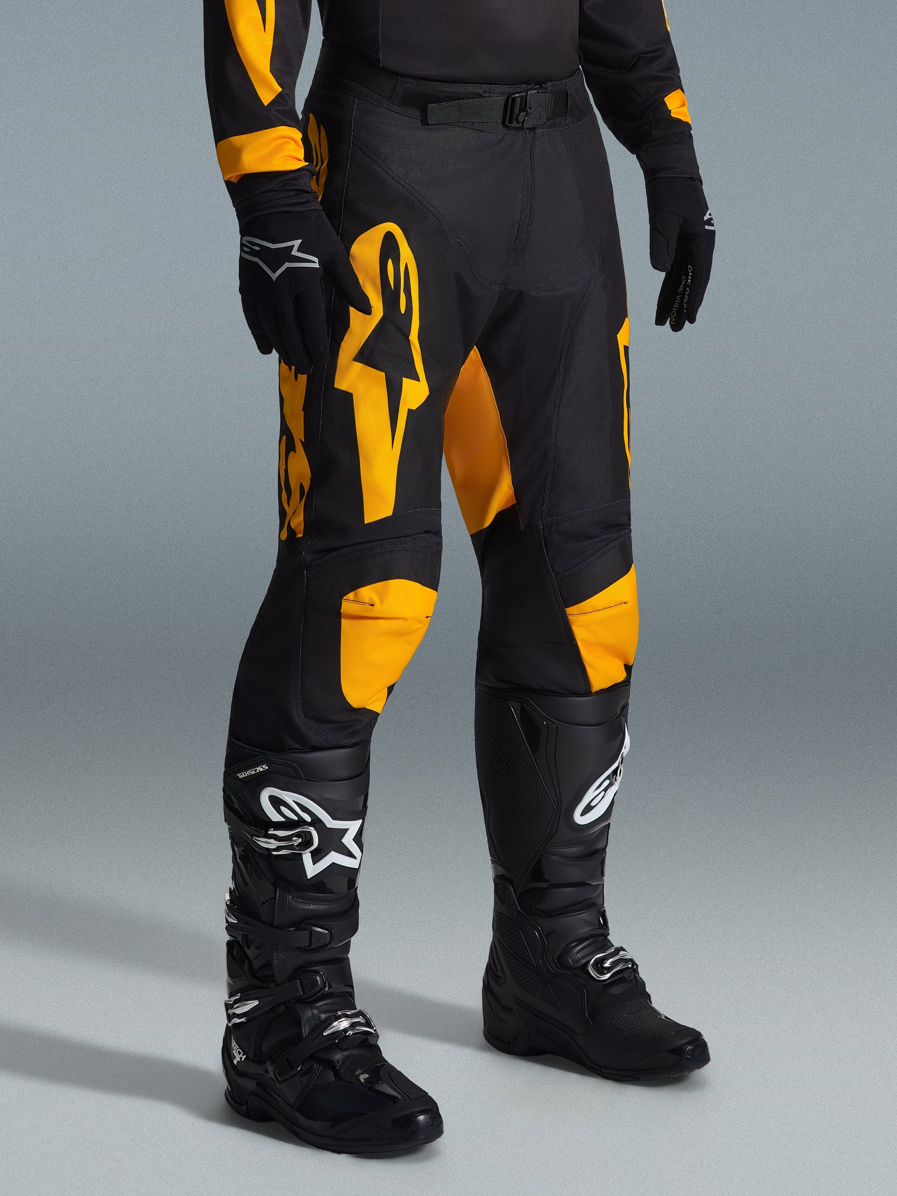 Calças Alpinestars Racer Riway 2026, calças de motocross, amarelas e pretas, usadas com luvas pretas e botas de motocross pretas, com logótipos Alpinestars em amarelo vibrante e detalhes nos joelhos sobre uma base preta, concebidas para corridas todo-o-terreno de alta performance
