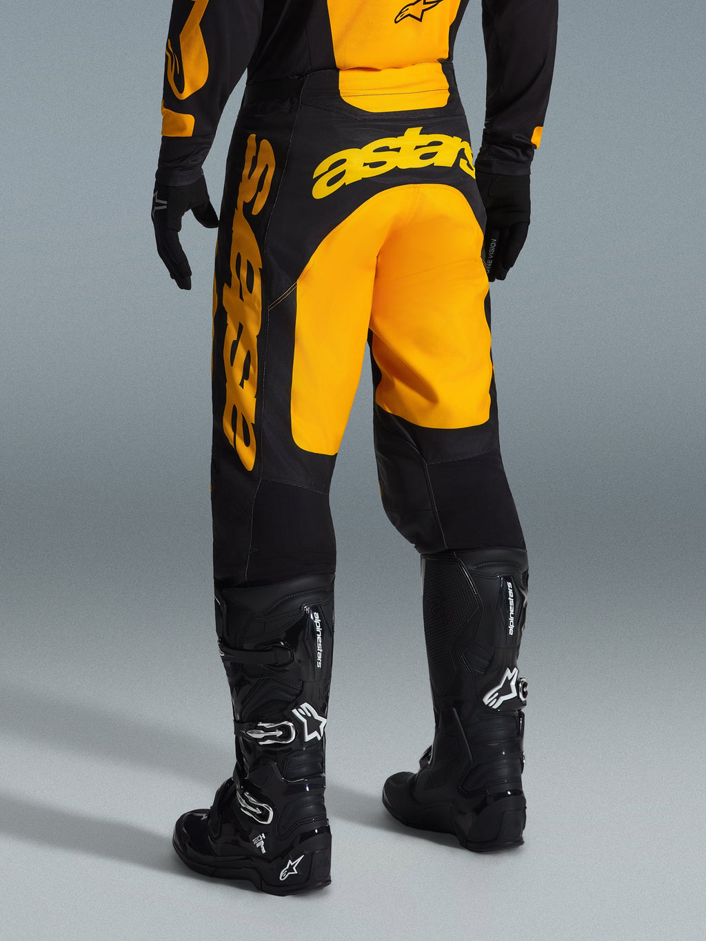 Calças Alpinestars 2026 Racer Riway, calças de motocross, amarelas e pretas, vista traseira mostrando a marca astars em destaque a amarelo no assento e na perna, combinadas com botas e luvas de motocross pretas