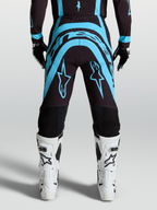 Alpinestars Calças Supertech Vesta, calças de motocross para homem, preto e turquesa com botas todo-o-terreno brancas, vista traseira, ajuste de corrida racing fit