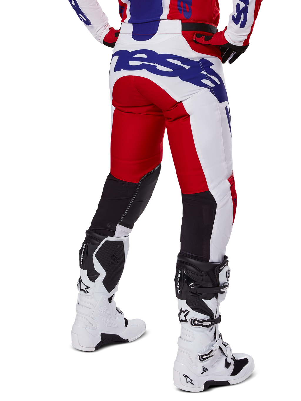 Alpinestars 2025 Racer Veil Pants, calças de motocross, vermelho vivo e branco com logótipos azuis, vista traseira com painéis de ventilação elásticos pretos na parte de trás das pernas, combinadas com botas de motocross brancas.