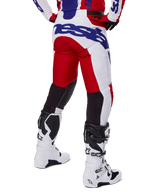 Alpinestars 2025 Racer Veil Pants, calças de motocross, vermelho vivo e branco com logótipos azuis, vista traseira com painéis de ventilação elásticos pretos na parte de trás das pernas, combinadas com botas de motocross brancas.