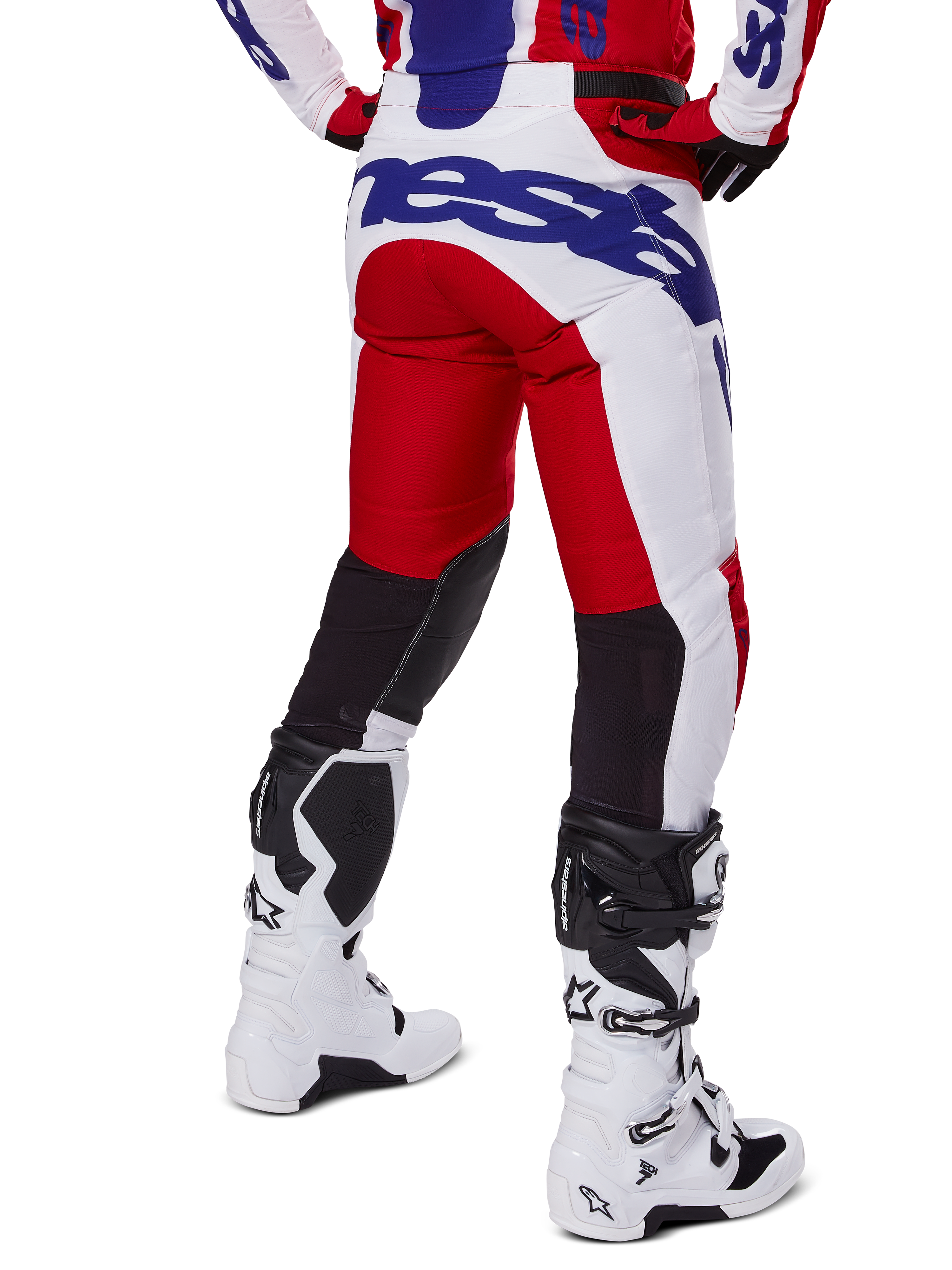 Alpinestars 2025 Racer Veil Pants, calças de motocross, vermelho vivo e branco com logótipos azuis, vista traseira com painéis de ventilação elásticos pretos na parte de trás das pernas, combinadas com botas de motocross brancas.