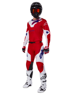 Alpinestars 2025 Racer Veil Pants, calças de motocross, vermelho vivo e branco, usadas como parte de um conjunto completo de equipamento de corrida que inclui uma camisola vermelha e branca a condizer, capacete preto com óculos cor de laranja, botas brancas e luvas vermelhas, apresentando logótipos Alpinestars azuis em destaque