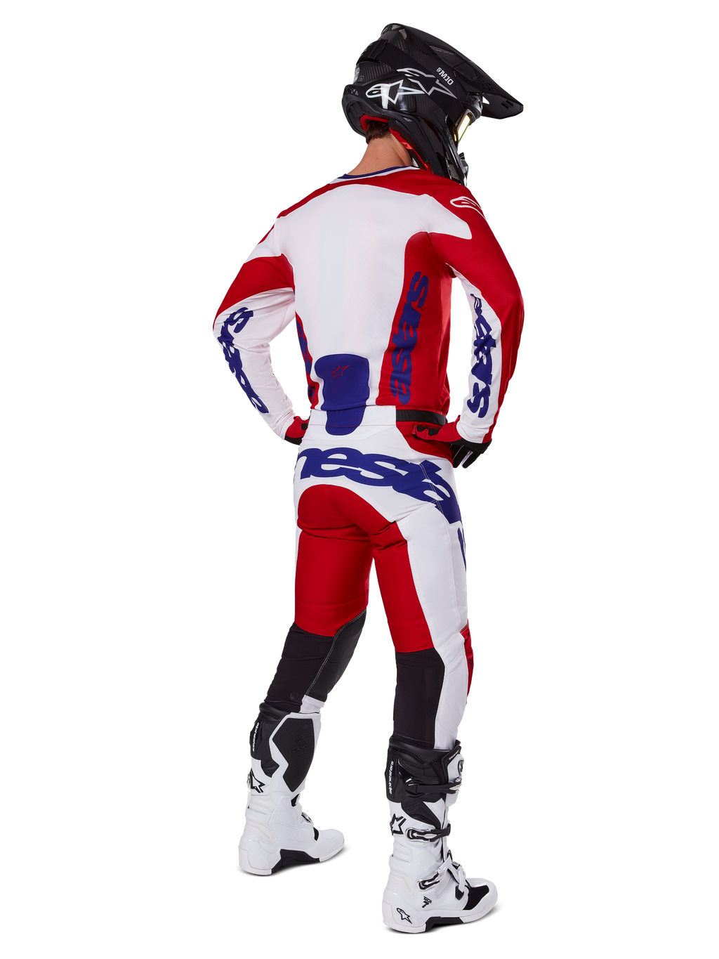 Alpinestars 2025 Racer Veil Pants, calças de motocross, vermelho vivo e branco com detalhes em azul, vistas de trás num piloto com equipamento completo, com o logótipo Alpinestars em destaque, painéis respiráveis na parte inferior das pernas, botas brancas e capacete preto coordenados