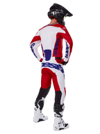 Alpinestars 2025 Racer Veil Pants, calças de motocross, vermelho vivo e branco com detalhes em azul, vistas de trás num piloto com equipamento completo, com o logótipo Alpinestars em destaque, painéis respiráveis na parte inferior das pernas, botas brancas e capacete preto coordenados